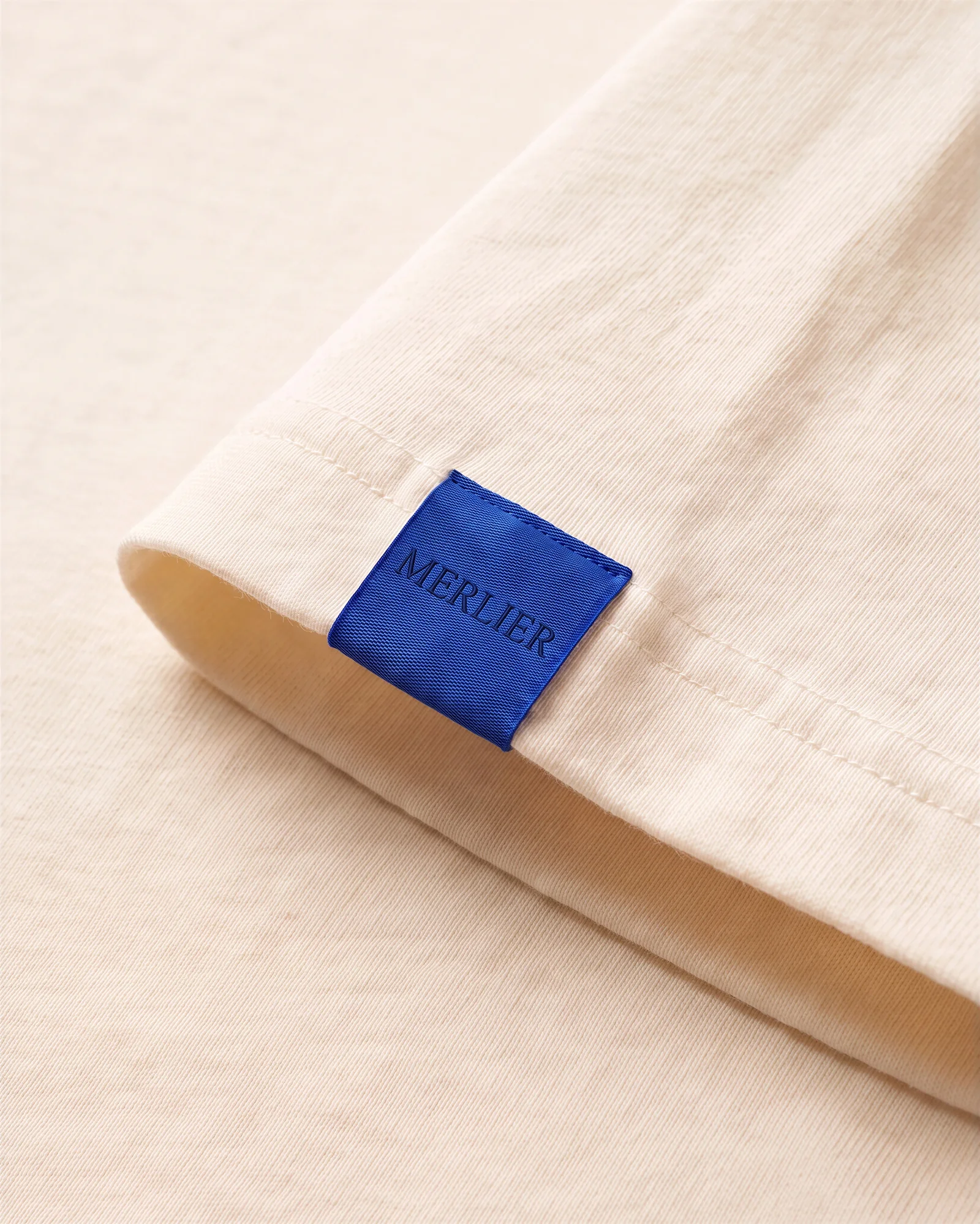 The cobalt MERLIER tag at the sleeve hem.